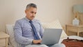 Young hispanic man business worker using laptop sitting on bed at hotel room Royalty Free Stock Photo