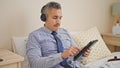 Young hispanic man business worker using touchpad and headphones sitting on bed at hotel room Royalty Free Stock Photo