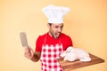 Young hispanic man cooking chicken holding knife angry and mad screaming frustrated and furious, shouting with anger Royalty Free Stock Photo