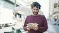 Young hispanic man counting denmark krone banknotes at coffee shop terrace