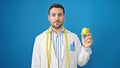 Young hispanic man dietician holding apple over isolated blue background