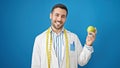 Young hispanic man dietician smiling confident holding apple over isolated blue background