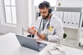 Young hispanic man doctor listening to music writing medical report at clinic