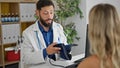 Young hispanic man doctor measuring patient pulse using arm tensiometer at the clinic