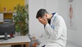 Young hispanic man doctor sitting on massage board stressed at the clinic