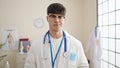 Young hispanic man doctor standing with serious expression at clinic