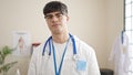 Young hispanic man doctor standing with serious expression at clinic