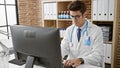 Young hispanic man doctor using computer working at the clinic Royalty Free Stock Photo