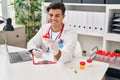 Young hispanic man doctor writing medical report holding urine test tube at clinic Royalty Free Stock Photo