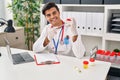 Young hispanic man doctor writing medical report holding urine test tube at clinic Royalty Free Stock Photo