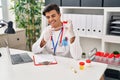 Young hispanic man doctor writing medical report holding urine test tube at clinic Royalty Free Stock Photo