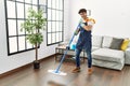 Young hispanic man doing chores singing using mop as a microphone at home Royalty Free Stock Photo