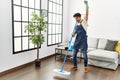 Young hispanic man doing chores singing using mop as a microphone at home Royalty Free Stock Photo