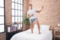 Young hispanic man doing guitar gesture standing on bed at bedroom Royalty Free Stock Photo