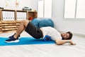 Young hispanic man doing rehab using foam roller at clinic