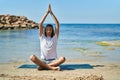 Young hispanic man doing yoga exercise sitting on sand at beach Royalty Free Stock Photo