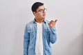 Young hispanic man with down syndrome wearing casual denim jacket over white background pointing thumb up to the side smiling Royalty Free Stock Photo