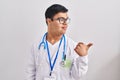 Young hispanic man with down syndrome wearing doctor uniform and stethoscope smiling with happy face looking and pointing to the Royalty Free Stock Photo