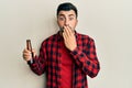 Young hispanic man drinking a bottle of beer covering mouth with hand, shocked and afraid for mistake Royalty Free Stock Photo