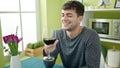 Young hispanic man drinking glass of wine sitting on table at dinning room Royalty Free Stock Photo