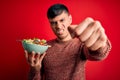 Young hispanic man eating vegetarian healthy salad over red isolated background annoyed and frustrated shouting with anger, crazy