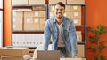 Young hispanic man ecommerce business worker smiling confident standing by laptop at office Royalty Free Stock Photo