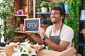 Young hispanic man florist smiling confident holding open blackboard at flower shop