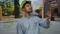 Young hispanic man with hardhat using tablet in outdoor park setting, demonstrating modern technology use in construction Royalty Free Stock Photo