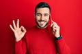 Young hispanic man having conversation talking on the smartphone doing ok sign with fingers, smiling friendly gesturing excellent Royalty Free Stock Photo