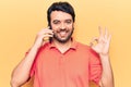 Young hispanic man having conversation talking on the smartphone doing ok sign with fingers, smiling friendly gesturing excellent Royalty Free Stock Photo