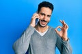 Young hispanic man having conversation talking on the smartphone doing ok sign with fingers, smiling friendly gesturing excellent Royalty Free Stock Photo