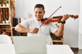 Young hispanic man having online violin lesson using laptop sitting on the table at home