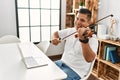 Young hispanic man having online violin lesson using laptop sitting on the table at home