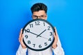 Young hispanic man holding big clock over face depressed and worry for distress, crying angry and afraid Royalty Free Stock Photo