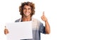 Young hispanic man holding blank empty banner smiling happy and positive, thumb up doing excellent and approval sign