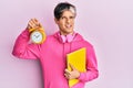 Young hispanic man holding book and alarm clock clueless and confused expression Royalty Free Stock Photo