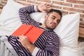 Young hispanic man holding book lying on bed sleeping at bedroom Royalty Free Stock Photo