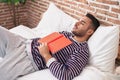 Young hispanic man holding book lying on bed sleeping at bedroom Royalty Free Stock Photo