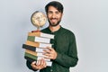 Young hispanic man holding books and world ball smiling with a happy and cool smile on face Royalty Free Stock Photo