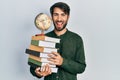 Young hispanic man holding books and world ball smiling and laughing hard out loud because funny crazy joke Royalty Free Stock Photo