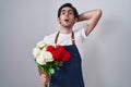 Young hispanic man holding bouquet of white and red roses crazy and scared with hands on head, afraid and surprised of shock with Royalty Free Stock Photo