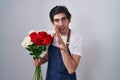 Young hispanic man holding bouquet of white and red roses hand on mouth telling secret rumor, whispering malicious talk