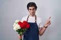 Young hispanic man holding bouquet of white and red roses pointing with hand finger to the side showing advertisement, serious and Royalty Free Stock Photo