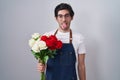 Young hispanic man holding bouquet of white and red roses sticking tongue out happy with funny expression