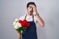 Young hispanic man holding bouquet of white and red roses yawning tired covering half face, eye and mouth with hand Royalty Free Stock Photo