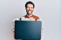 Young hispanic man holding briefcase with dollars sticking tongue out happy with funny expression Royalty Free Stock Photo
