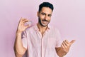 Young hispanic man holding brilliant diamond stone pointing thumb up to the side smiling happy with open mouth Royalty Free Stock Photo