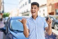 Young Hispanic Man Holding Car Key Pointing Thumb Up To The Side Smiling Happy With Open Mouth