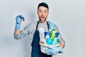 Young hispanic man holding cleaning products and cockroach afraid and shocked with surprise and amazed expression, fear and