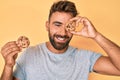 Young hispanic man holding cookie winking looking at the camera with sexy expression, cheerful and happy face Royalty Free Stock Photo